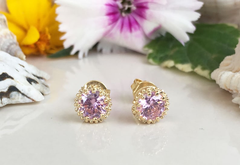 Puede incluir: Un par de pendientes de bot&oacute;n de oro con un centro de piedra preciosa rosa y un halo de cuentas.