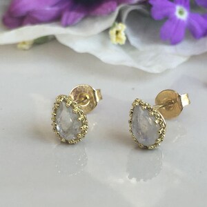May include: A pair of gold earrings with a pear-shaped moonstone set in a delicate gold frame.