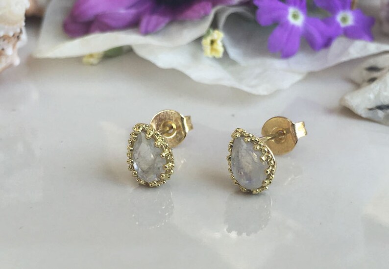 May include: A pair of gold earrings with a pear-shaped moonstone set in a delicate gold frame.