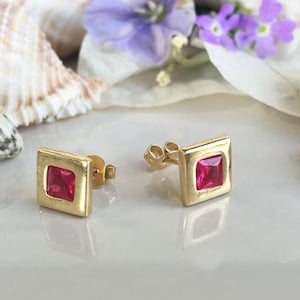 May include: A pair of gold square-shaped earrings with a pink gemstone in the centre of each earring.