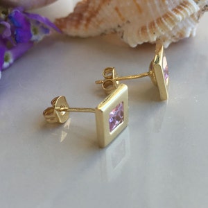 May include: A pair of gold earrings with square pink gemstones.