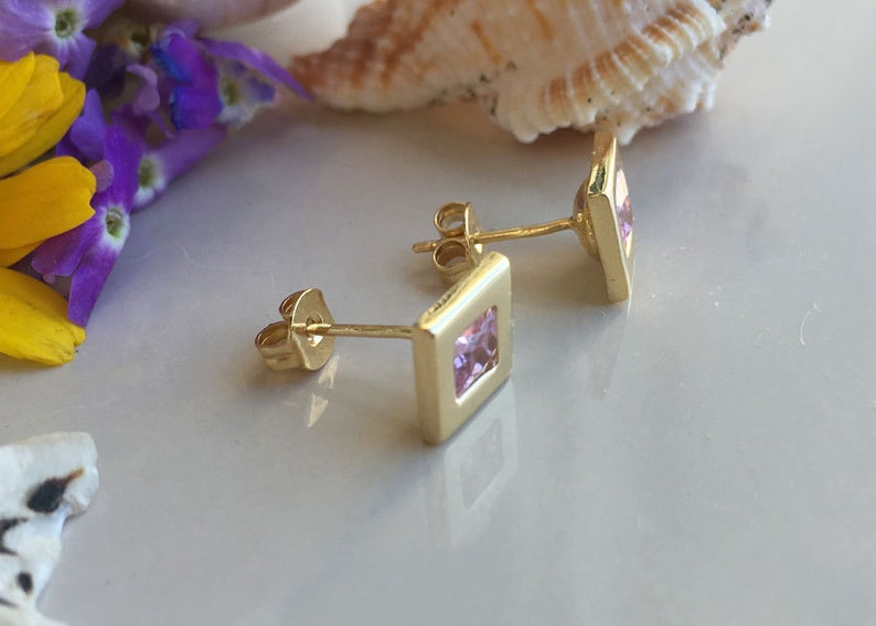 May include: A pair of gold earrings with square pink gemstones.
