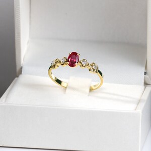 May include: A gold ring with a red oval gemstone and smaller white gemstones set in a delicate band.