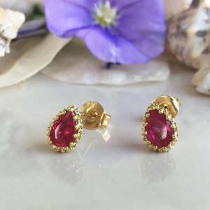 May include: A pair of gold earrings with a teardrop-shaped red gemstone set in a gold filigree design.