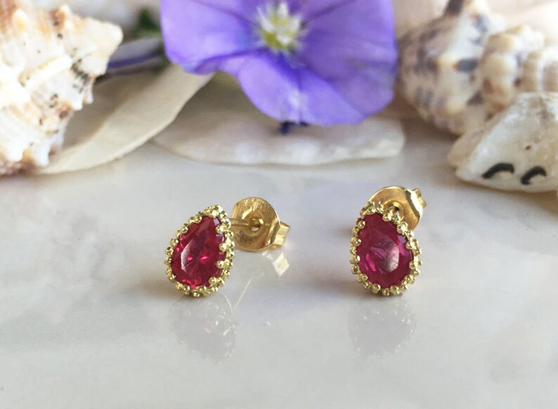 May include: A pair of gold earrings with a teardrop-shaped red gemstone set in a gold filigree design.