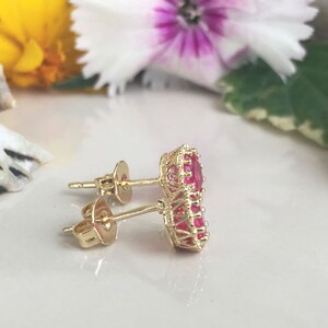 May include: A pair of gold earrings with red gemstone accents. The earrings have a simple post design and feature a cluster of red gemstones in a circular shape.