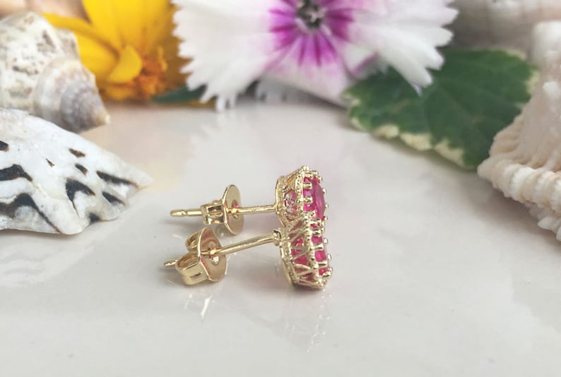 May include: A pair of gold earrings with red gemstone accents. The earrings have a simple post design and feature a cluster of red gemstones in a circular shape.
