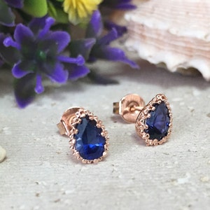 Puede incluir: Un par de pendientes de oro rosa con una piedra preciosa azul en forma de pera engastada en un delicado bisel festoneado.