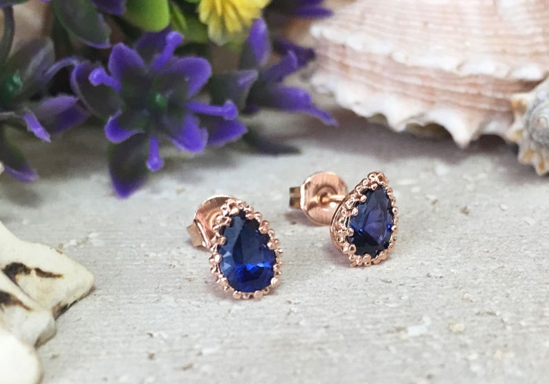 Puede incluir: Un par de pendientes de oro rosa con una piedra preciosa azul en forma de pera engastada en un delicado bisel festoneado.