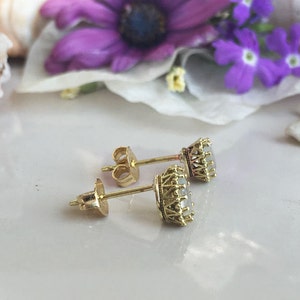 May include: A pair of gold earrings with a white stone set in a crown-shaped setting.