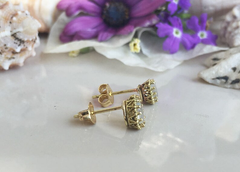 May include: A pair of gold earrings with a white stone set in a crown-shaped setting.