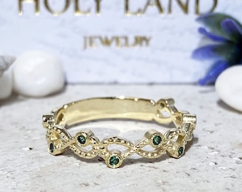 Puede incluir: Un anillo de banda de oro con un diseño delicado e intrincado que presenta una serie de bucles conectados. El anillo está adornado con cinco pequeñas piedras preciosas de color verde esmeralda.