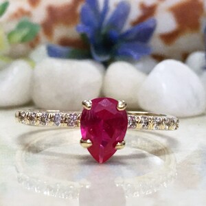 Op de afbeelding: Een gouden ring met een peervormige robijn, omringd door een band van kleine diamanten.
