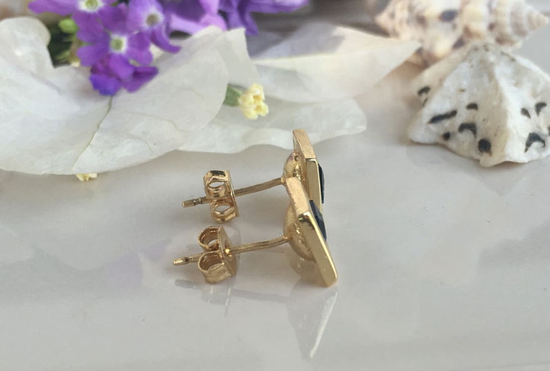 May include: A pair of gold earrings with black square-shaped stones. The earrings have a post and butterfly back.