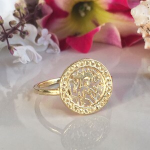 May include: Gold ring with a circular design featuring a cutout of a tree. The ring is on a white surface.