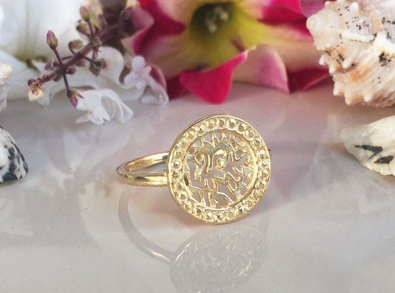 May include: Gold ring with a circular design featuring a cutout of a tree. The ring is on a white surface.