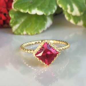 May include: A gold ring with a twisted band and a square-shaped red gemstone.