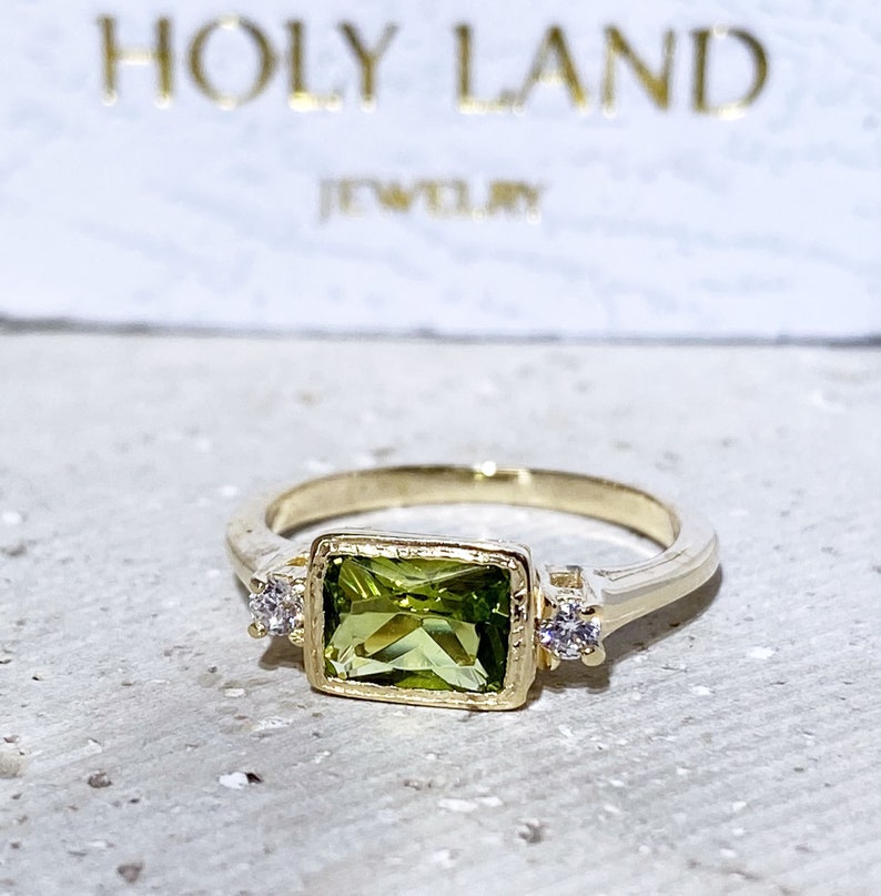 This gorgeous and elegant women's ring features an octagon-cut natural peridot gemstone with two round-cut dazzling clear quartz. This beautiful ring is enhanced with a high polish finish.