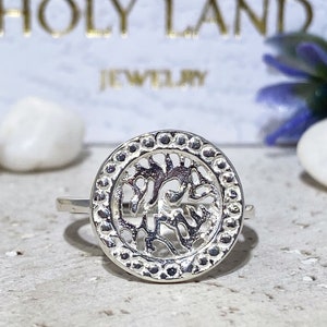 May include: A silver ring with a circular design featuring a tree of life motif. The ring has a beaded edge.