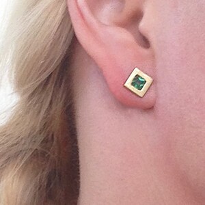 May include: A pair of gold square earrings with a small green gemstone in the center.