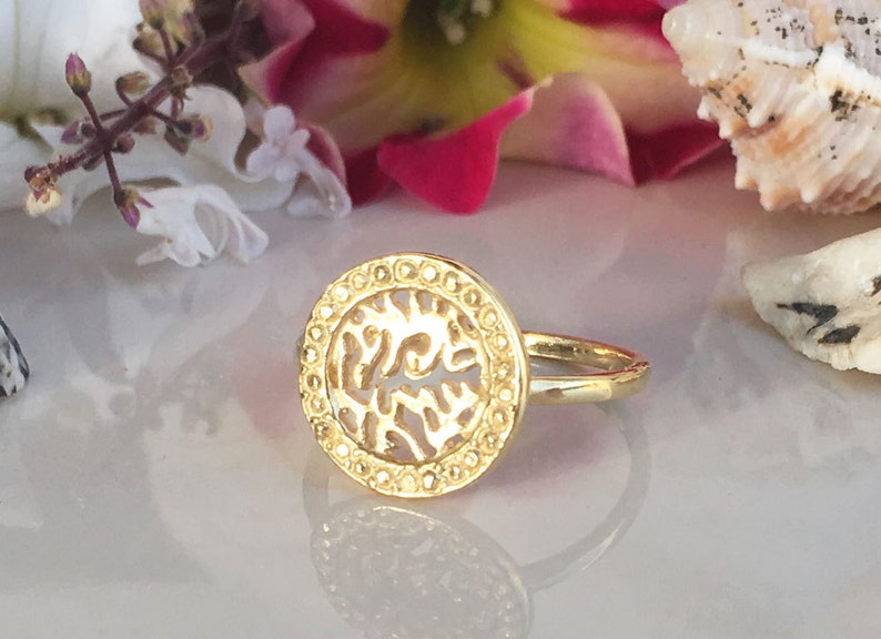 May include: A gold ring with a circular design featuring a cutout pattern. The ring is on a white surface.