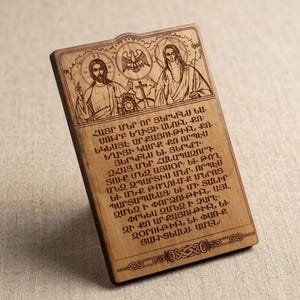 May include: A rectangular wooden plaque featuring a laser-engraved depiction of two figures with halos, a central eagle emblem, and a cross. Below the imagery, the plaque displays a block of Armenian text, with a decorative border at the bottom.