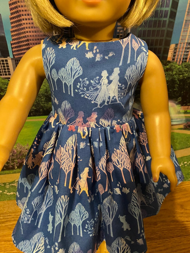 May include: A blue sleeveless dress with a white and purple floral pattern featuring silhouettes of characters from the film Frozen. The dress has a gathered skirt and a scoop neckline.