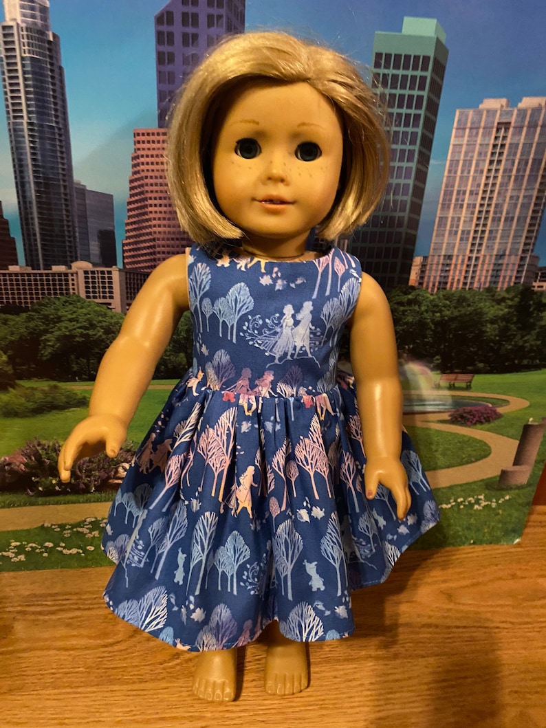 May include: A blue dress with a white and pink floral pattern featuring characters from the film Frozen. The dress is sleeveless and has a gathered skirt.