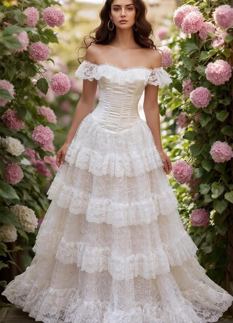 May include: A white off-the-shoulder dress featuring a fitted bodice and a multi-tiered skirt. The garment is constructed with intricate lace detailing, including ruffled lace trim along the neckline and horizontal lace layers on the skirt.