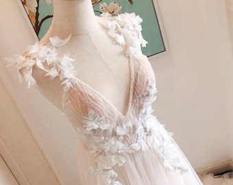 Pode incluir: Um vestido de noiva branco com decote profundo e aplicações florais. O vestido tem um corpete transparente e uma saia fluida.