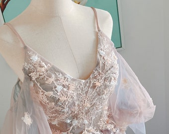 May include: A blush pink tulle dress with delicate floral embroidery and a V-neckline. The dress has a sheer overlay with puff sleeves.