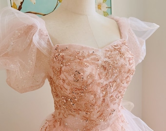 May include: A pink tulle dress with a sweetheart neckline and puff sleeves. The bodice is embellished with a floral pattern of sequins and beads.