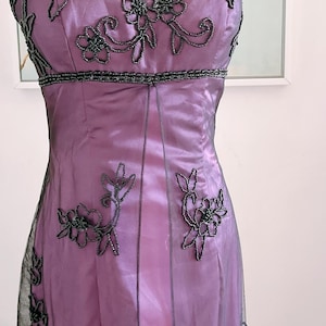 May include: A formal, strapless, lavender-colored dress. The bodice and waistline are embellished with dark gray beading. Floral beaded designs cascade down the front of the dress. The dress is made of a shiny, silky material and has a sheer overlay.