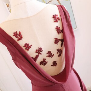 May include: Burgundy sleeveless dress with a sheer back panel featuring red floral embellishments.