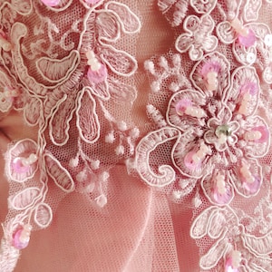 May include: Pink lace fabric with delicate floral embroidery and pink sequins. The fabric has a soft, flowing texture.