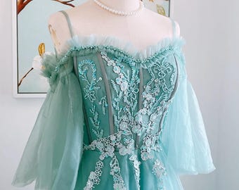 May include: A light blue off-the-shoulder dress with a lace bodice and tulle skirt. The dress is decorated with sequins and beads.