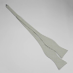 May include: A white and green striped bow tie. The bow tie is made of a soft, lightweight fabric.