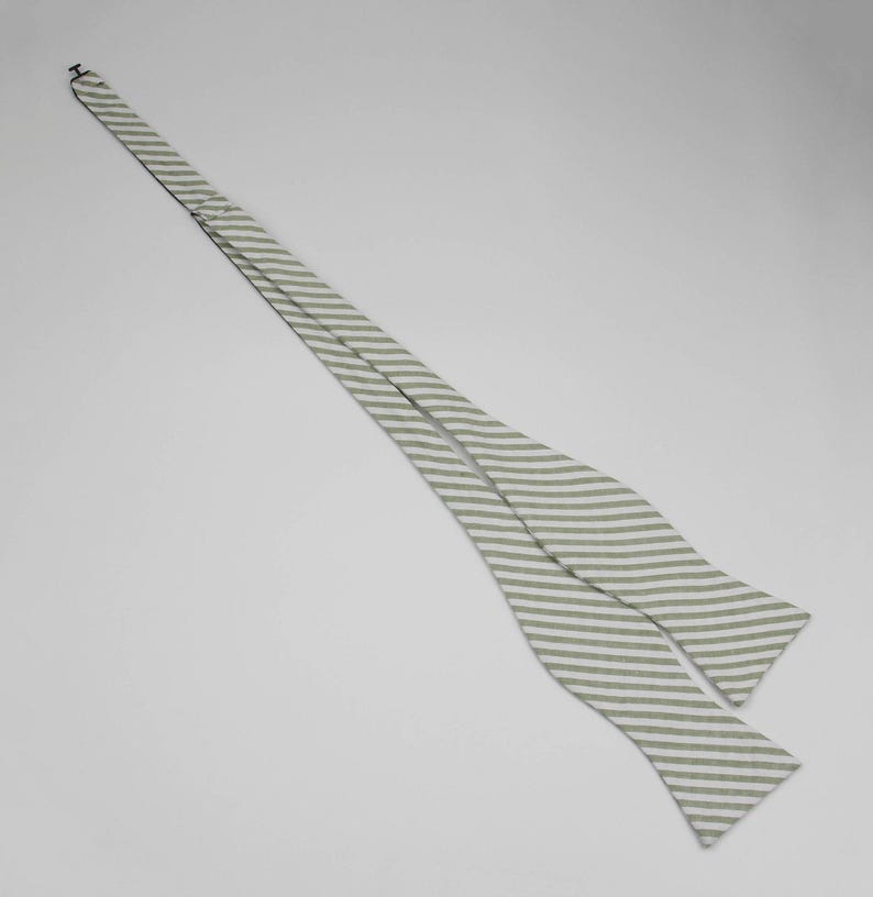 May include: A white and green striped bow tie. The bow tie is made of a soft, lightweight fabric.