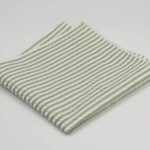May include: A white and green striped linen pocket square. The pocket square is folded in half and has a subtle texture.