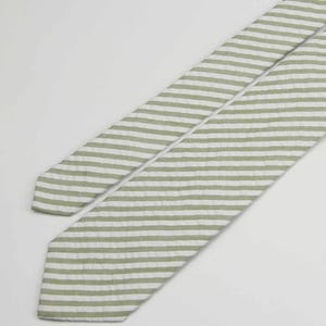 May include: A green and white striped tie. The tie is made of a soft, textured fabric.