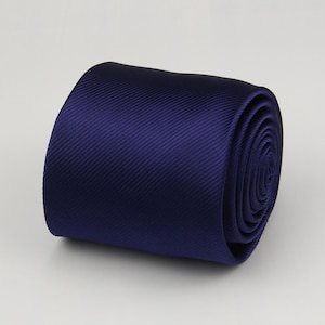Può includere: Cravatta blu navy arrotolata. La cravatta è realizzata in un tessuto liscio con una sottile trama a coste diagonali. Il colore blu scuro è uniforme su tutta la parte arrotolata della cravatta.