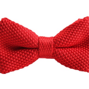 May include: A red knitted bow tie. The bow tie is made of a soft, textured fabric.