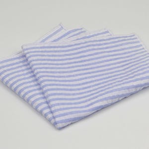 May include: A blue and white striped linen pocket square. The square is folded in half and the stripes are horizontal.