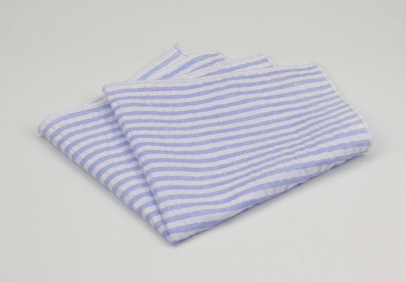 May include: A blue and white striped linen pocket square. The square is folded in half and the stripes are horizontal.