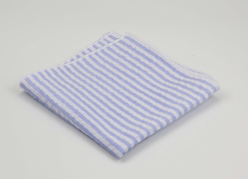 May include: A light blue and white striped pocket square. The pocket square is folded and has a white border.