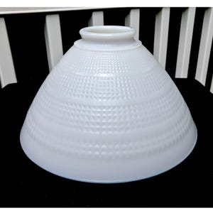 Op de afbeelding: Witte, gematte glazen lampenkap met een geometrisch patroon. De kap is kegelvormig en heeft een gladde, witte afwerking.