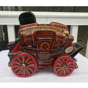 May include: A brown ceramic figurine of a stagecoach with a black top and red wheels. The stagecoach has the words "Overland Express" written on the side. The figurine is a vintage collectible.