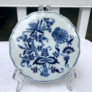 Può includere: Un piattino in porcellana bianca con un motivo floreale blu e bianco. Il piattino ha un bordo ondulato ed è decorato con un motivo floreale stilizzato.