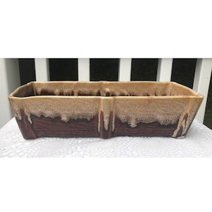 Könnte beinhalten: Ein rechteckiger Keramik-Pflanztopf mit zweifarbigem Glaze. Die obere Hälfte ist hellbraun und die untere Hälfte dunkelbraun. Der Pflanztopf hat einen strukturierten, getropften Glanzeffekt. Es ist ein Vintage-Stil.