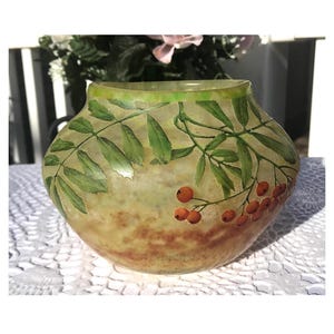 Puede incluir: Un jarrón de vidrio verde con un diseño floral marrón y naranja. El jarrón tiene una forma redondeada y una boca ancha.